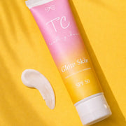 Tube of 'TC' Glow Skin sunscreen with a swatch on a yellow background
