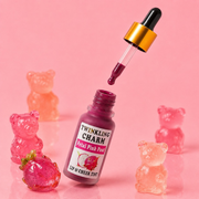 Lip and cheek tint bottle with a dropper and gummy bear toys on a pink background