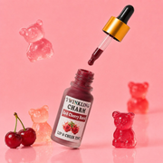 Lip and cheek tint bottle with dropper and gummy bear candies on a pink background