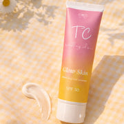 Tube of TC Glow Skin moisturizing facial sunscreen on a yellow textured background